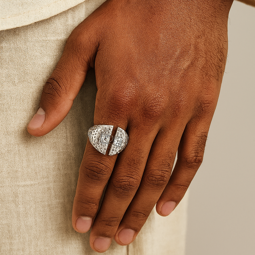 Hand wearing a silver signet ring with intricate design on a beige fabric background