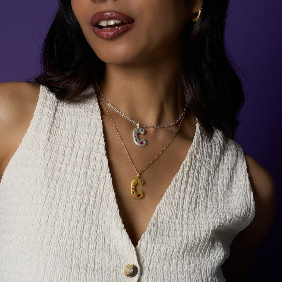 Woman wearing necklaces with 'C' pendants against a purple background