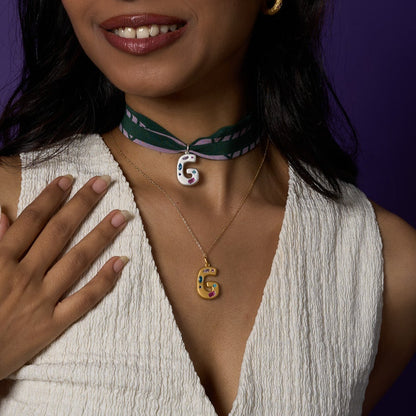 Woman wearing a white sleeveless top with buttons, gold necklace, and green choker against a purple background