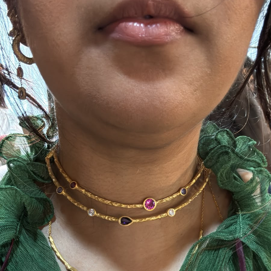 Close-up of a person wearing three layered gold necklaces with small gemstone accents, paired with a green sheer top.