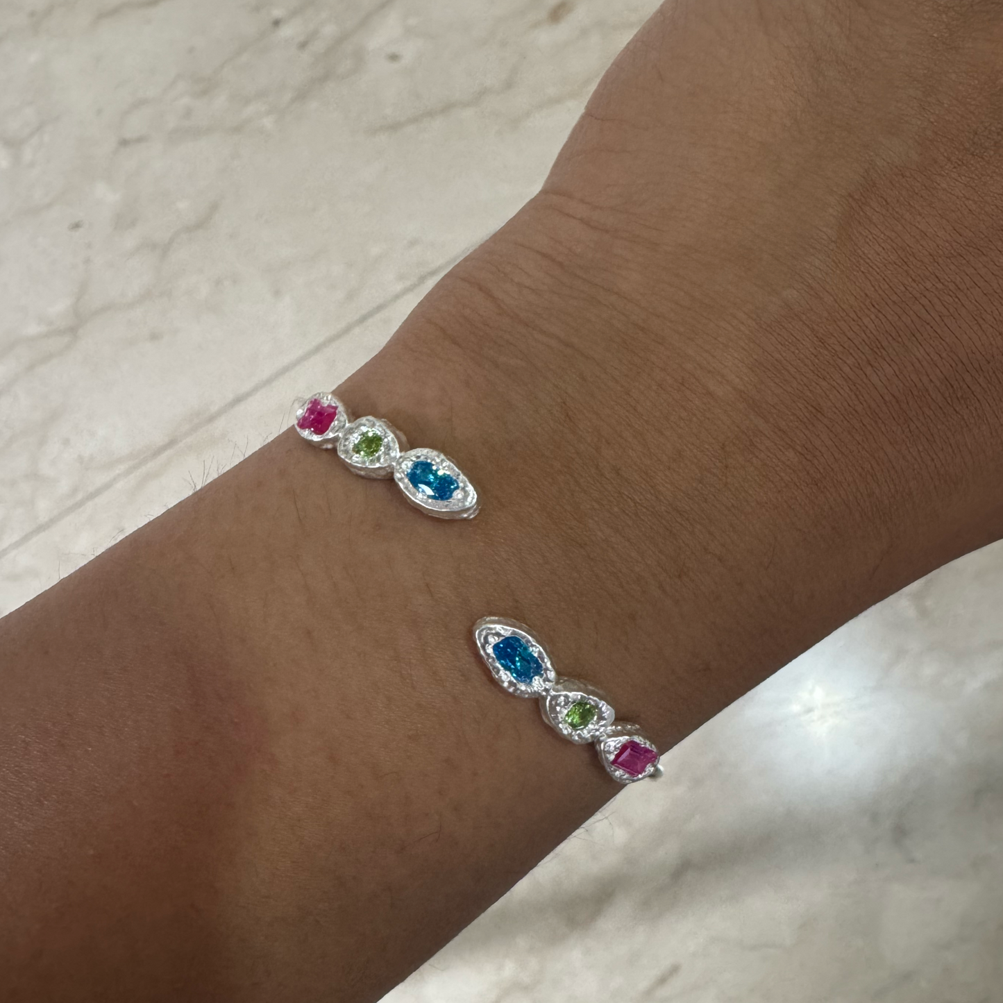 Bracelet with colorful gemstones on a wrist against a marble background
