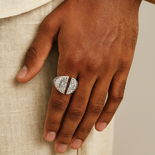 Hand wearing a silver signet ring with intricate design on a beige fabric background